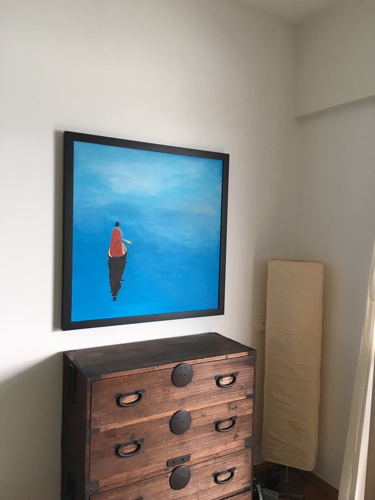 Painting of a monk in a red robe on a blue lake, hanging above a wooden chest