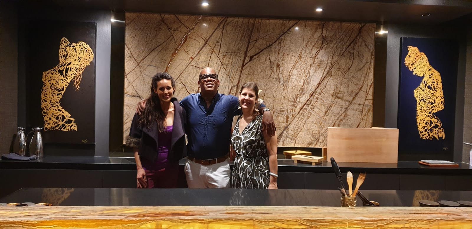 Raúl with two guests at a Japanese restaurant, his golden figure paintings on the walls